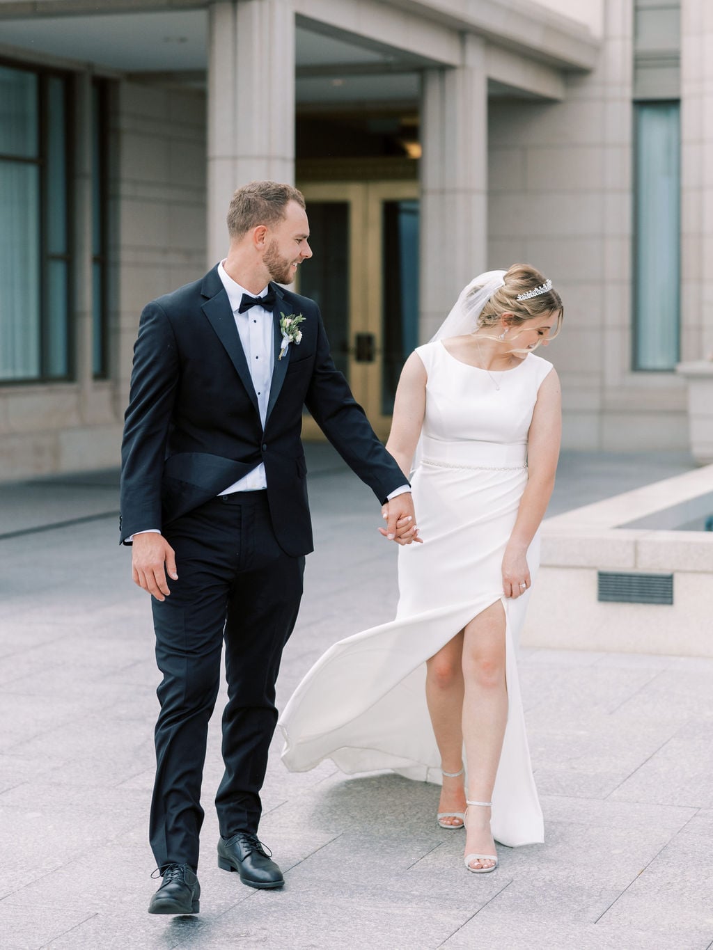 Joe and Holly walk hand in hand outside the temple, her dress catching the wind, Lehi, Utah