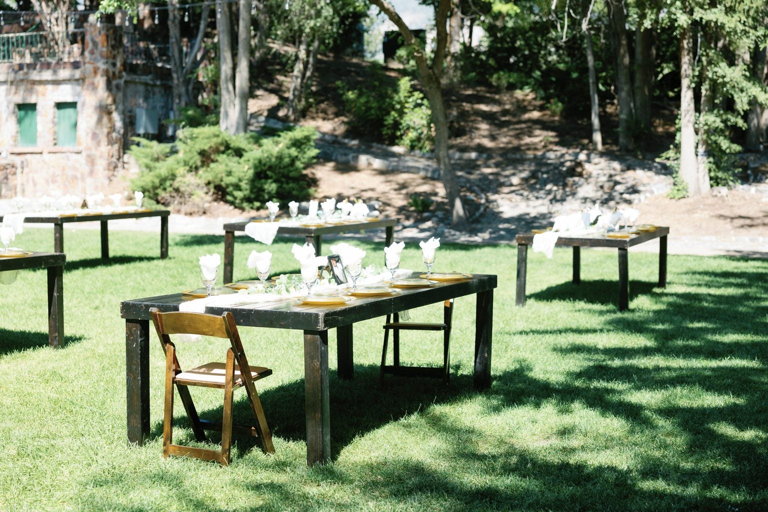 Long banquet tables set for dinner on the lawn beneath the trees, a private garden estate wedding in Utah