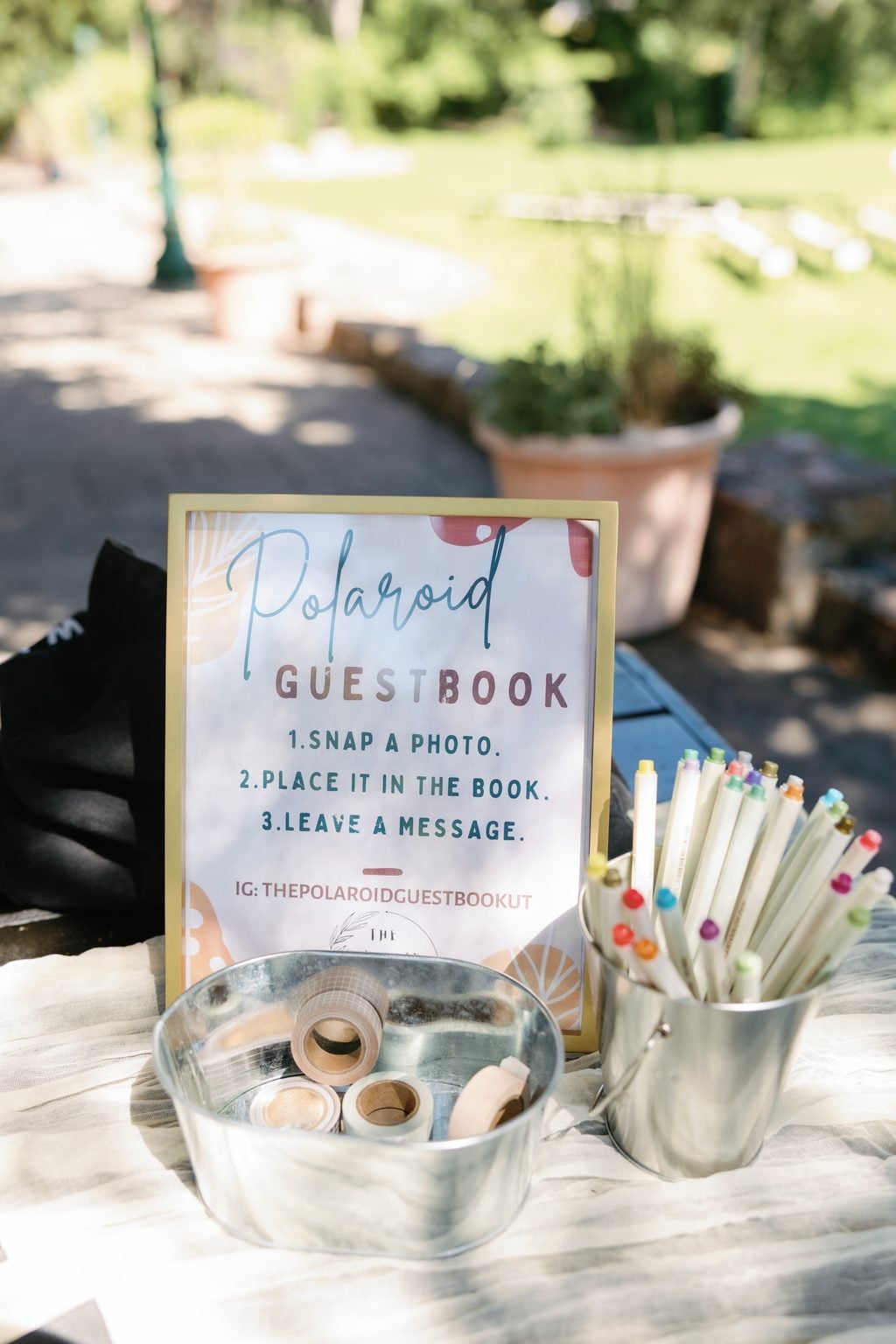 Polaroid guestbook sign and colored pens on the welcome table at Mallory and Saint's garden wedding