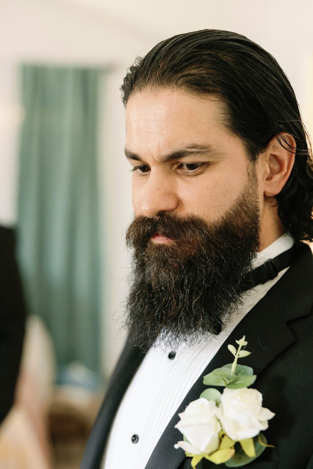 Portrait of the bearded groom in a black tuxedo with a white rose boutonniere