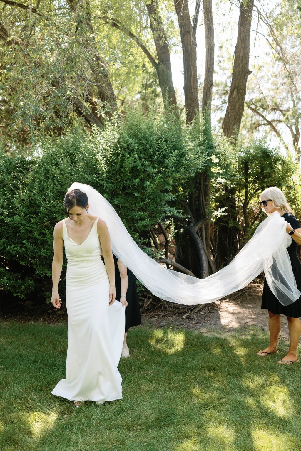 The bride from behind, her long veil trailing across the garden lawn, a Utah wedding