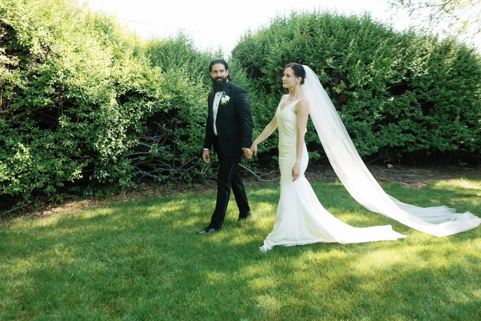 The couple walking the garden together, the bride's long veil catching the light