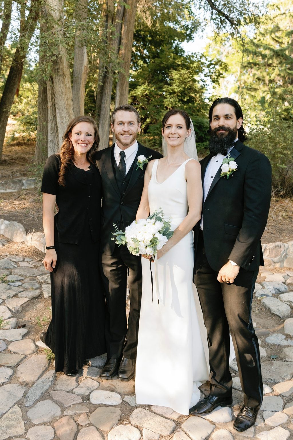 Mallory and Saint with their wedding party, all in black, beneath the trees