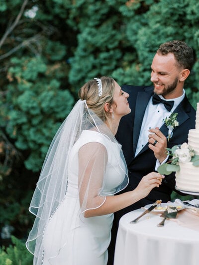 A bride and groom smile together while cutting their wedding cake at an outdoor Utah reception