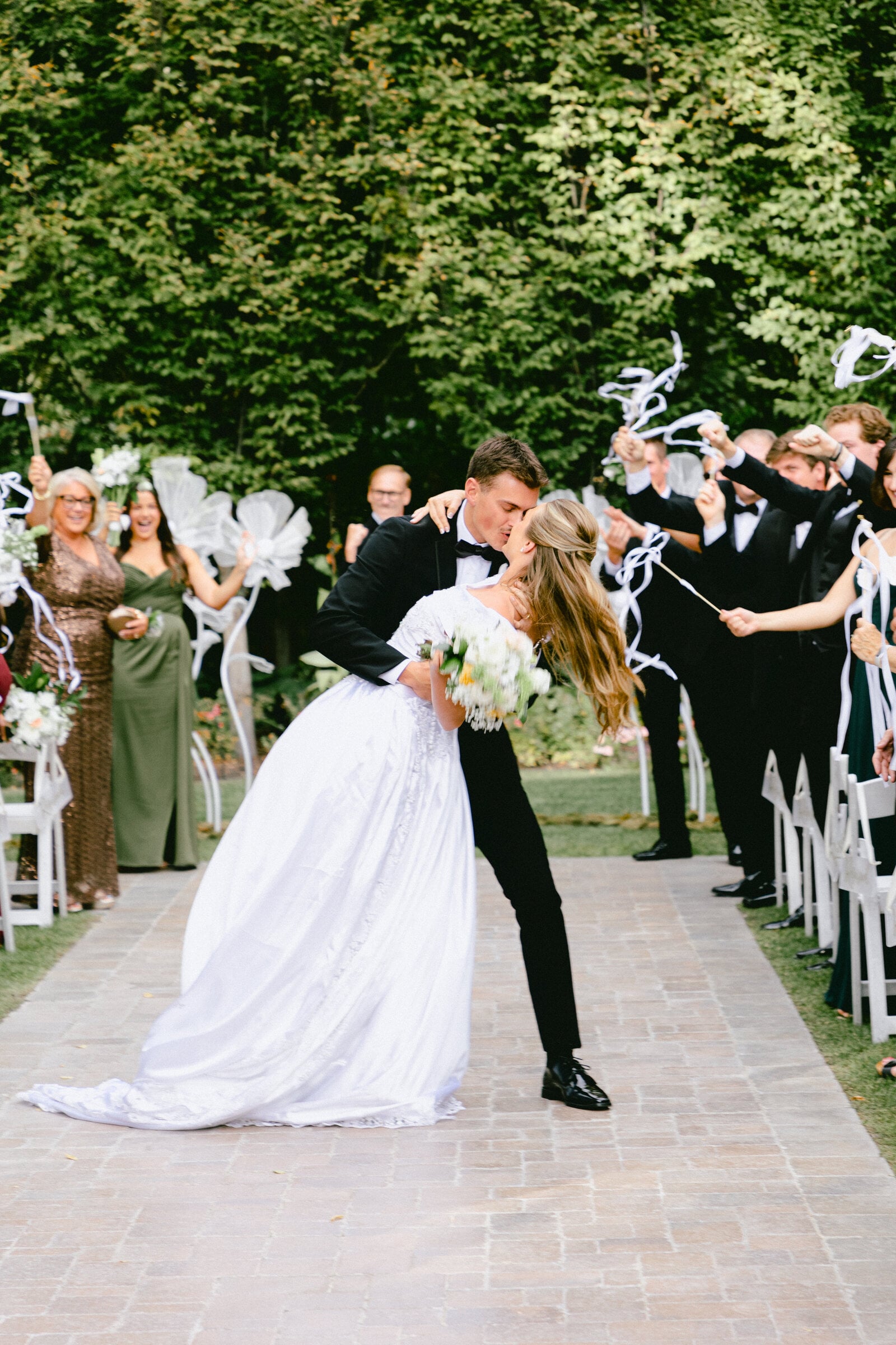 A couple kisses during their celebratory exit as guests cheer and wave ribbon wands at a Utah wedding